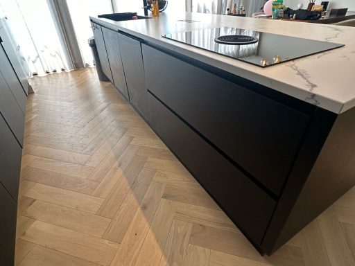 Zwarte moderne keuken met een marmeren werkblad en een houten visgraatvloer.
