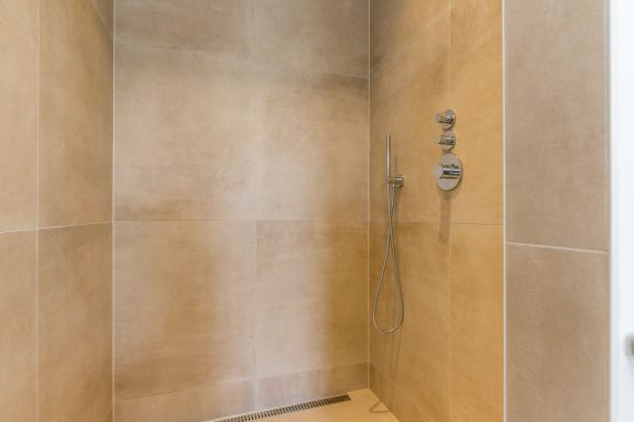 Moderne inloopdouche met beige tegels en dubbele douchesystemen.