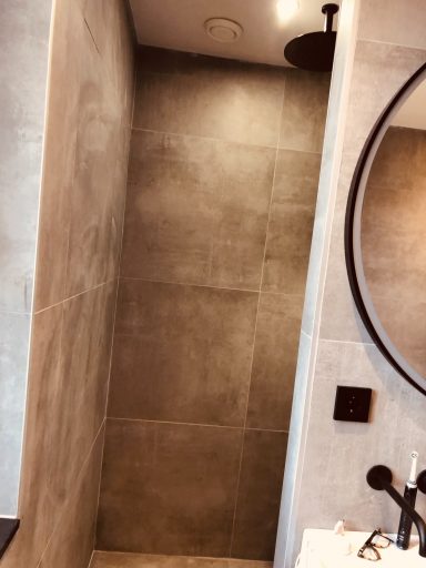 Moderne badkamer met een strakke, betegelde douchewand en ronde spiegel.