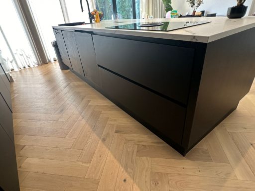 Zwarte keuken met een marmeren werkblad en een visgraatvloer.