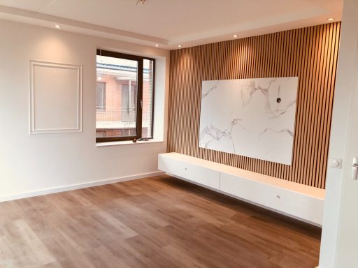 Moderne woonkamer met houten vloer en een lichte muur met decoratieve elementen.