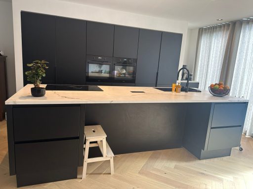 Moderne zwarte keuken met marmeren aanrecht en een klein krukje.