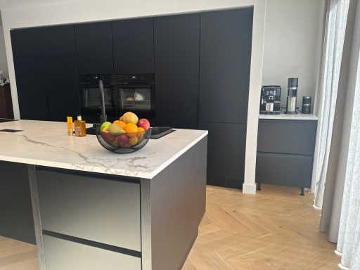 Moderne keuken met een schiereiland en een fruitschaal, zwarte kasten en houten vloer.