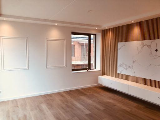 Lege moderne woonkamer met houten vloer, grote ramen en lichte wandafwerkingen.